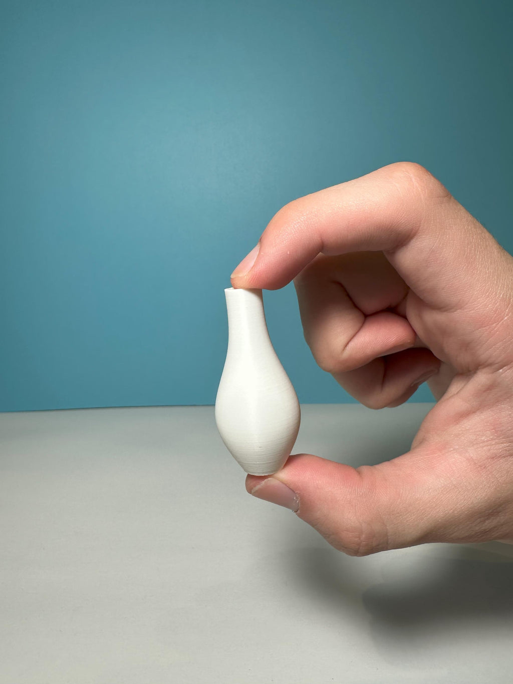 Hand holding a 1:12 scale miniature floor vase between two fingers to show its small size
